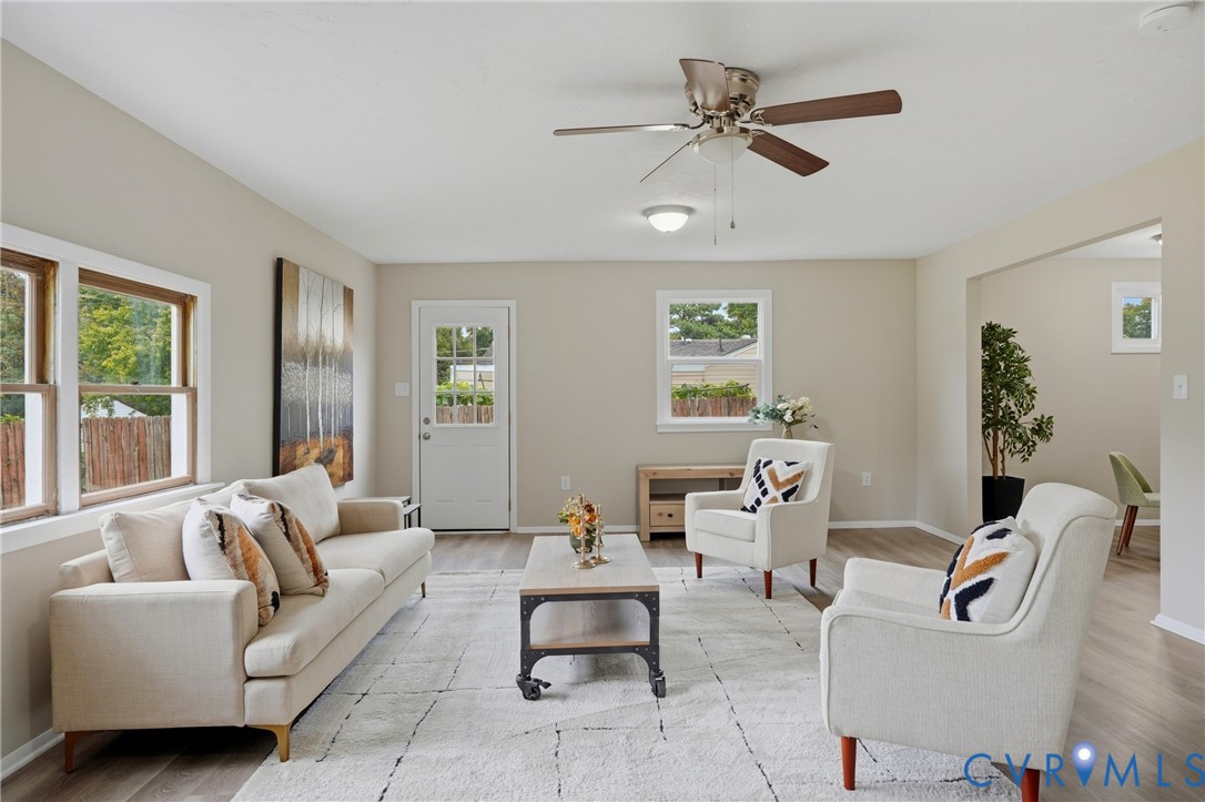 Vaulted ceiling with a ceiling fan, light wood-finish flooring, multiple windows, neutral wall tones, and an open doorway to an additional room