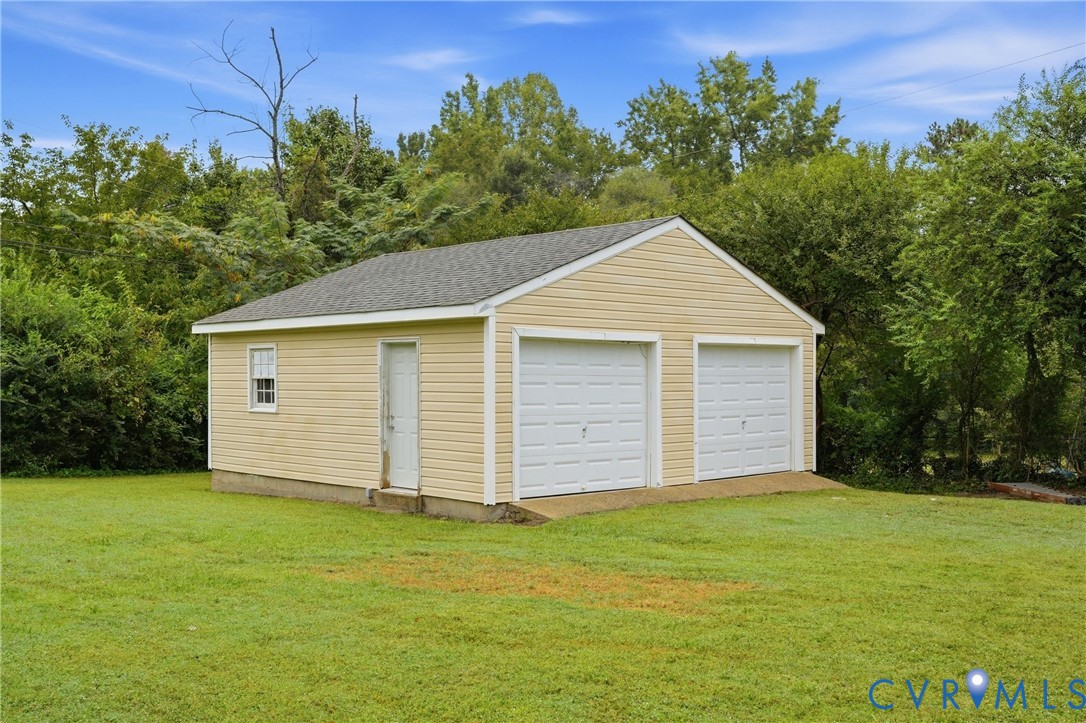 Detached two-car garage with light-colored siding and a dark shingle roof