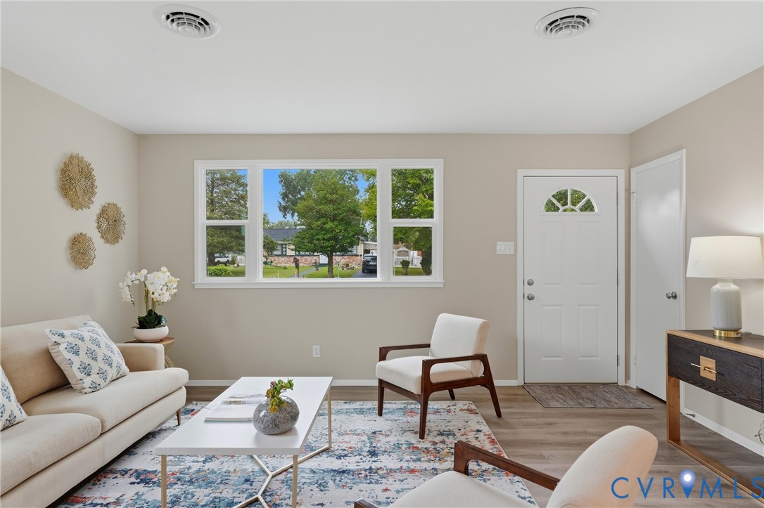 Wood-finish flooring throughout, multiple pane window, white entry door with decorative glass, and recessed ceiling vents