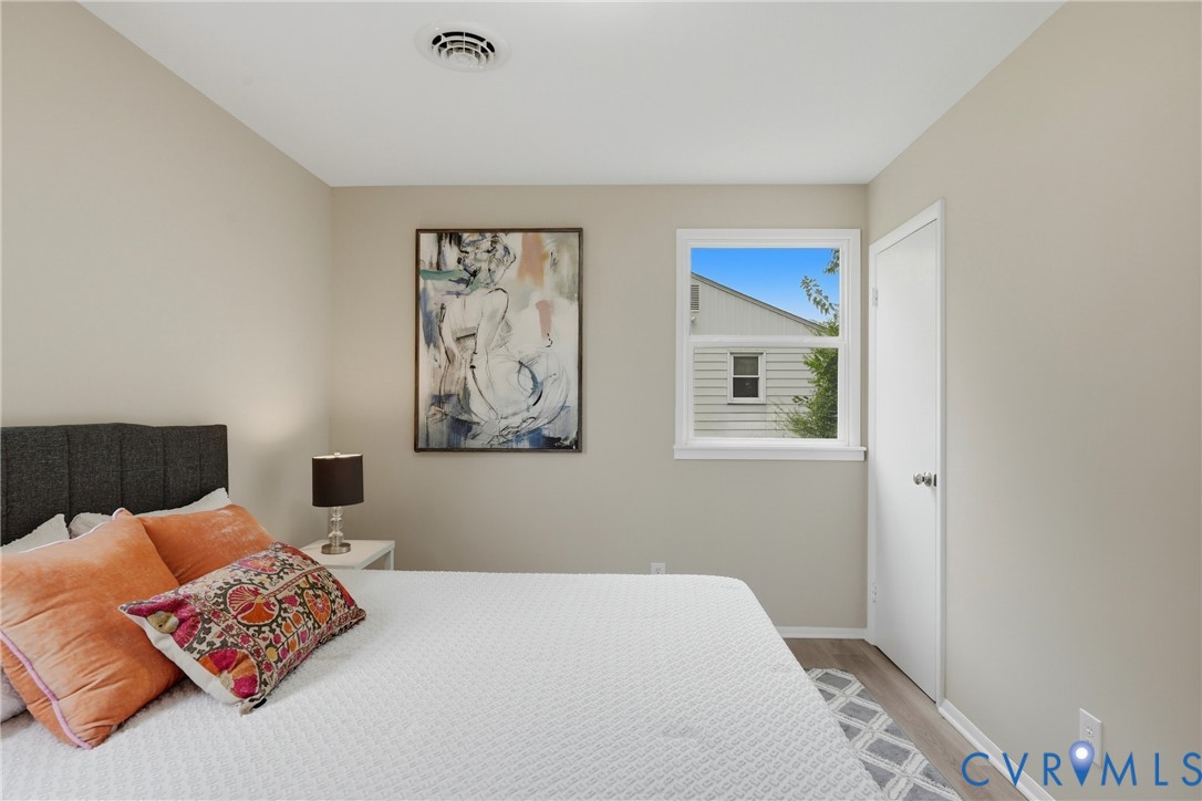 Neutral wall finishes, white trim, recessed ceiling vent, window with white frame, and wood-finish flooring
