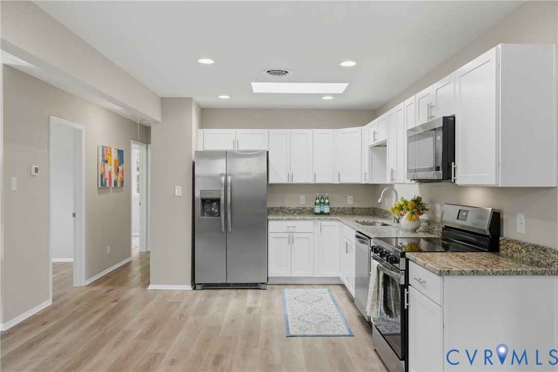 Kitchen featuring white cabinetry, stainless steel appliances, granite countertops, wood-finish flooring, and recessed lighting
