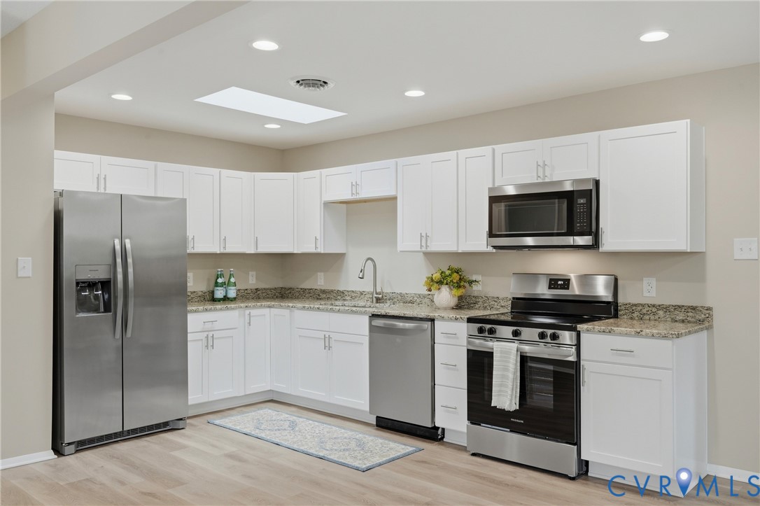 Kitchen featuring white cabinetry, stainless steel appliances, granite countertops, wood-finish flooring, and a skylight
