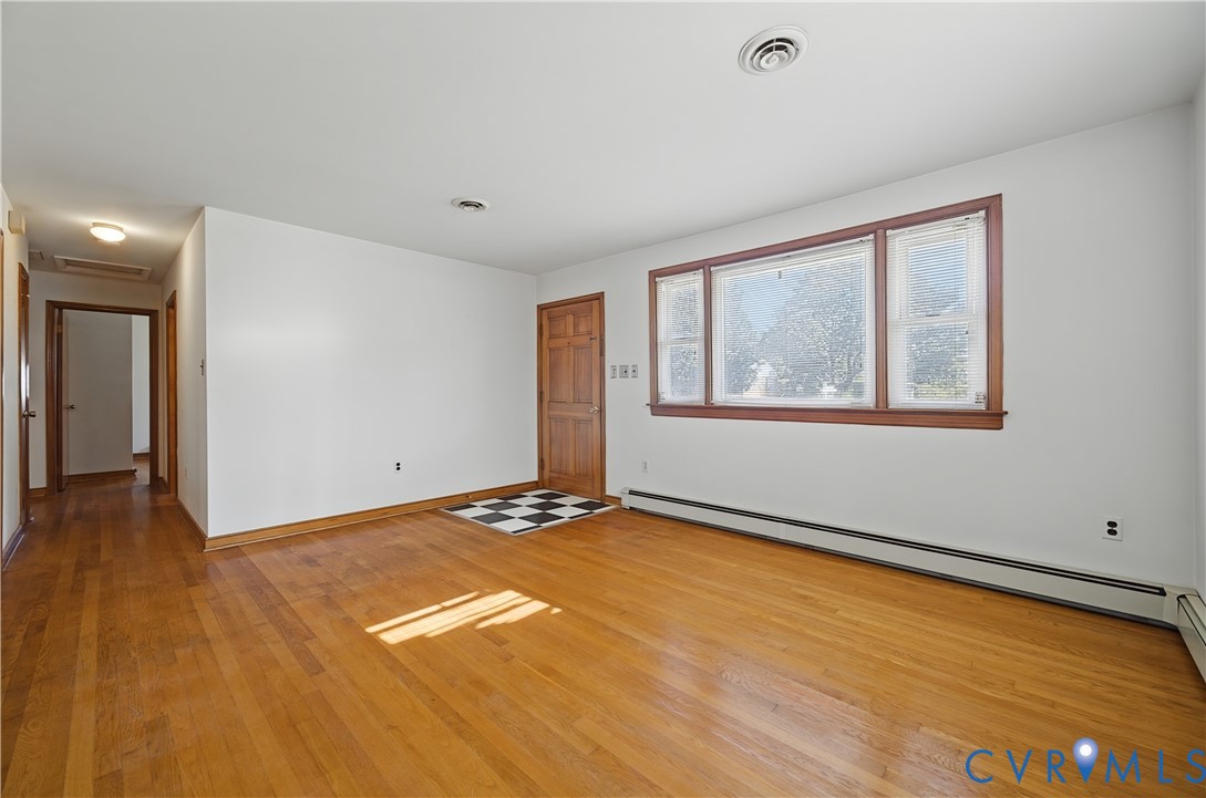 Spacious living area featuring warm wood-finish flooring, white walls, and large casement windows with wood frames
