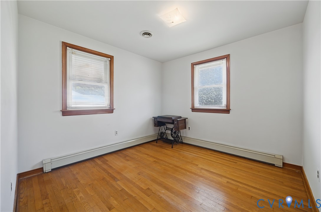 Bright corner room featuring gleaming hardwood flooring, two large double-hung windows with wood trim framing natural light, and clean white walls