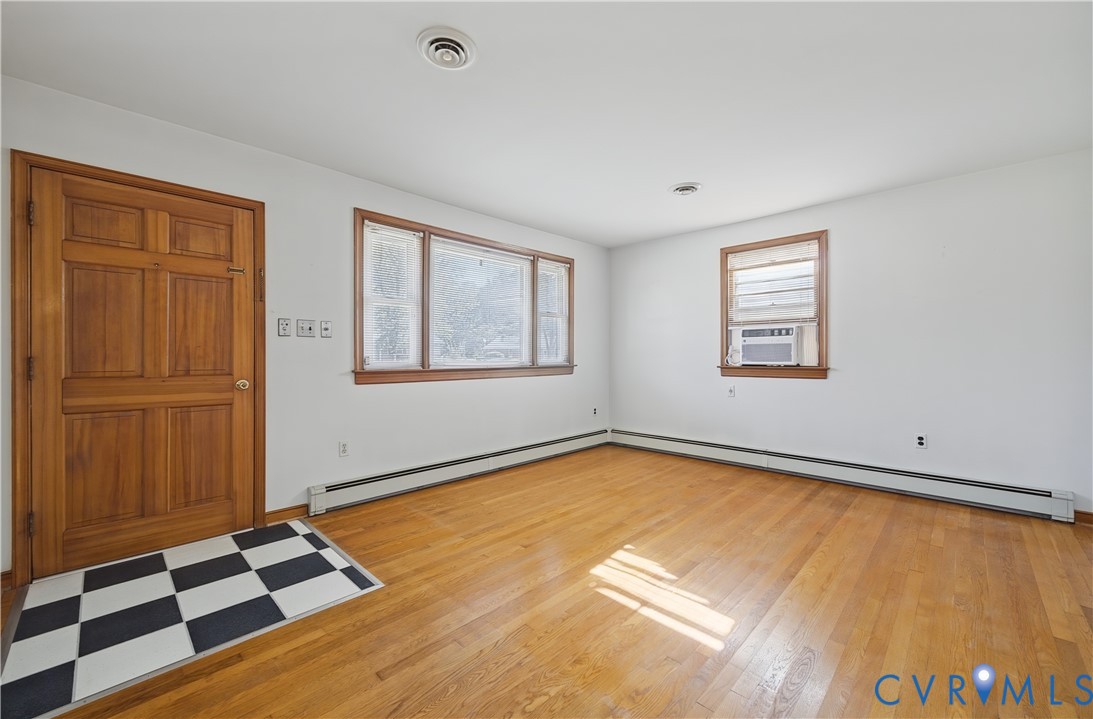 Hardwood flooring, wood panel door, multiple windows, window air conditioning unit, and white walls