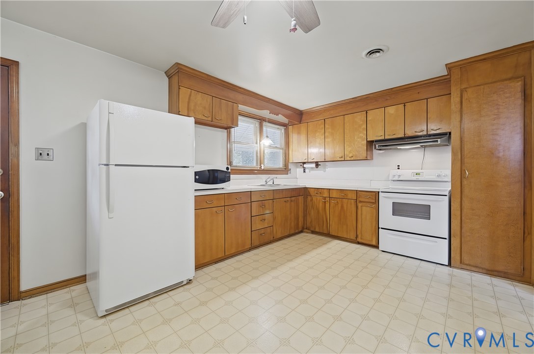 Wood cabinetry with white countertops, white range, and a ceiling fan with light fixture