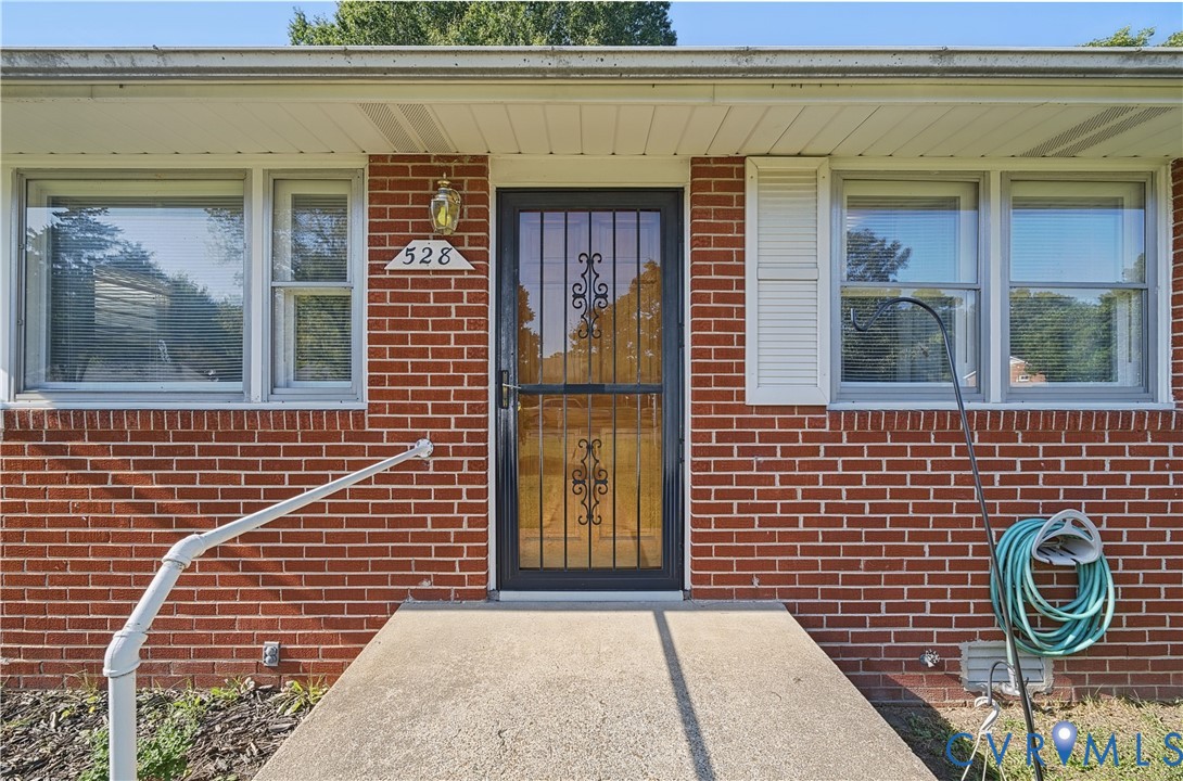 Red brick exterior featuring white window trim, white shutters, and a decorative storm door with ironwork