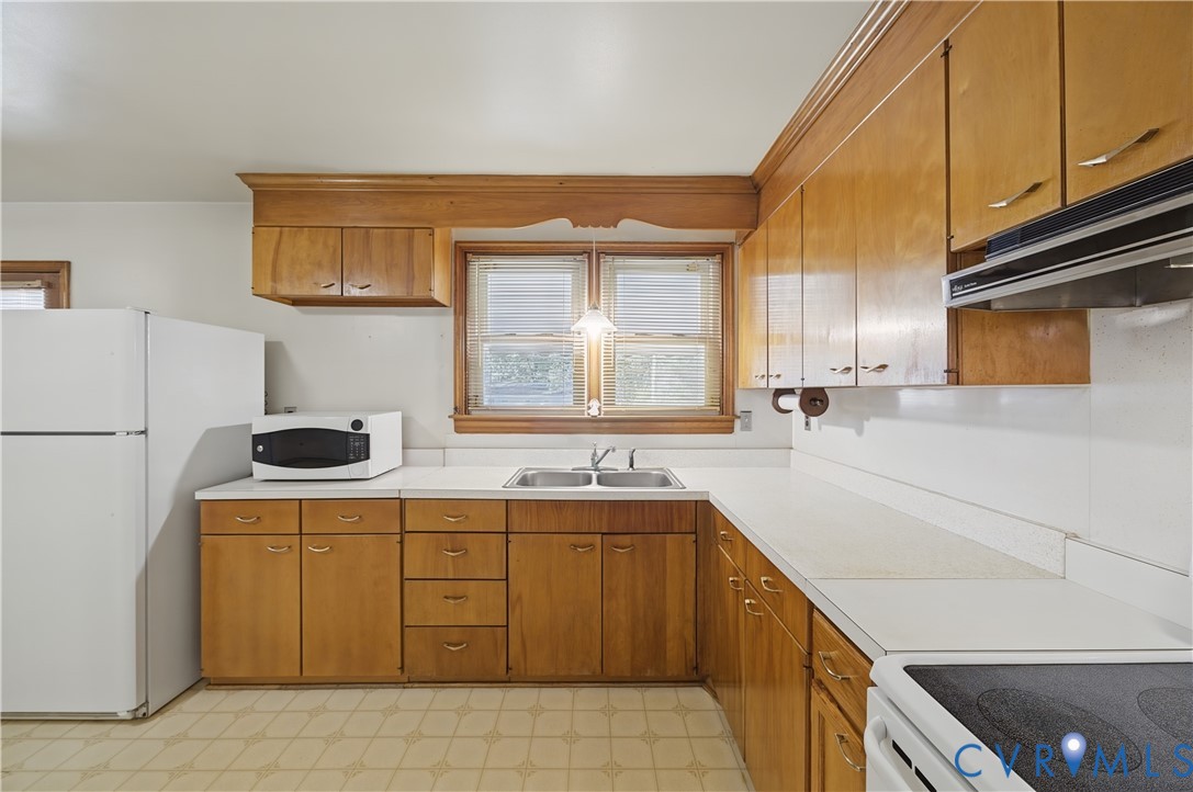 U-shaped kitchen layout with wood-finish cabinetry, white countertops, a double basin sink, and a built-in range hood