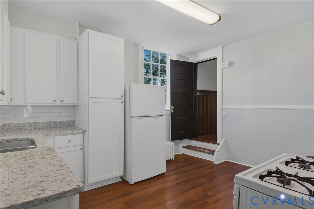 White cabinetry with silver-tone hardware, textured light-toned countertops, subway tile backsplash, and wood-finish flooring