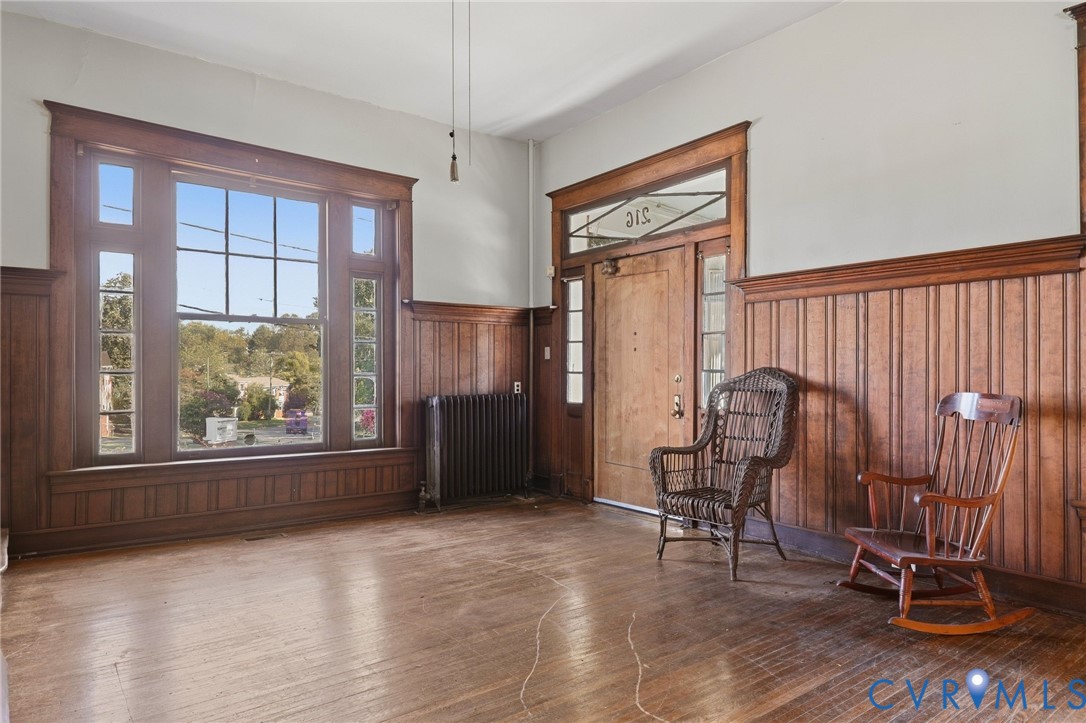 Hardwood flooring, wood paneling, decorative window trim, a prominent entry door with transom window, and a classic radiator Hardwood flooring, wood paneling, decorative window trim, a prominent entry door with transom window, and a classic radiator