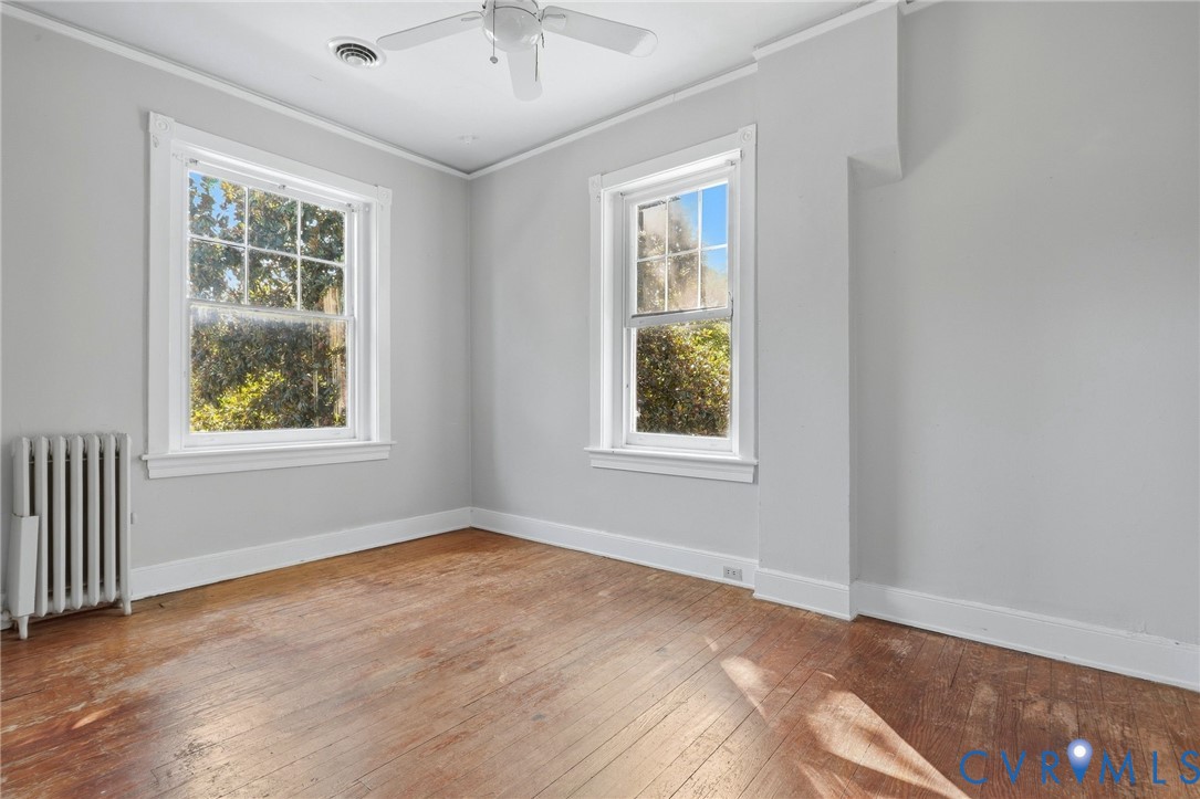 Hardwood flooring, painted walls, two large windows, white trim, and a ceiling fan