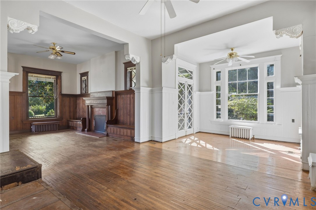 Wood-finish flooring throughout, featuring a substantial fireplace with an ornate mantel, extensive wood paneling, built-in window seating, and a large multi-pane window