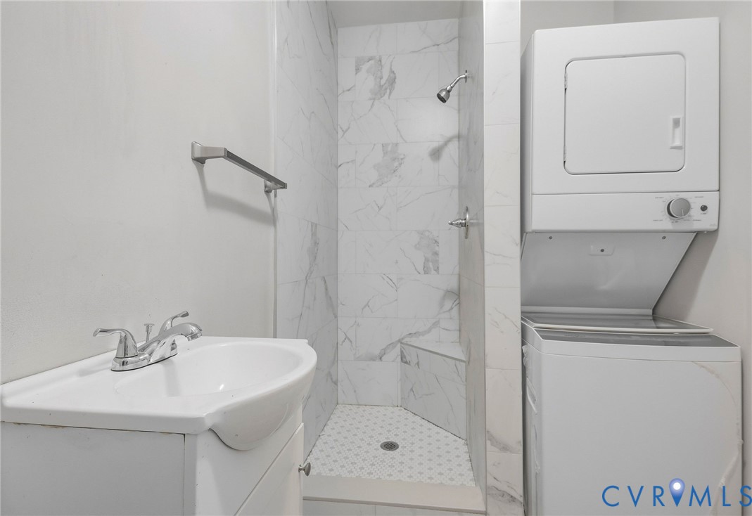 Corner sink vanity with chrome faucet, tiled shower with built-in bench, and stacked washer and dryer
