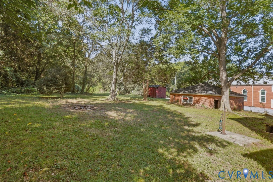 Expansive green space featuring a fire pit, mature trees, a red brick outbuilding, and a separate red shed