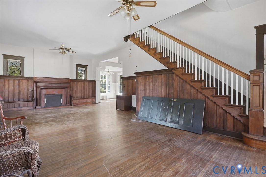 Hardwood flooring, wood paneling, ornate fireplace, staircase with white balusters, and ceiling fans Hardwood flooring, wood paneling, ornate fireplace, staircase with white balusters, and ceiling fans