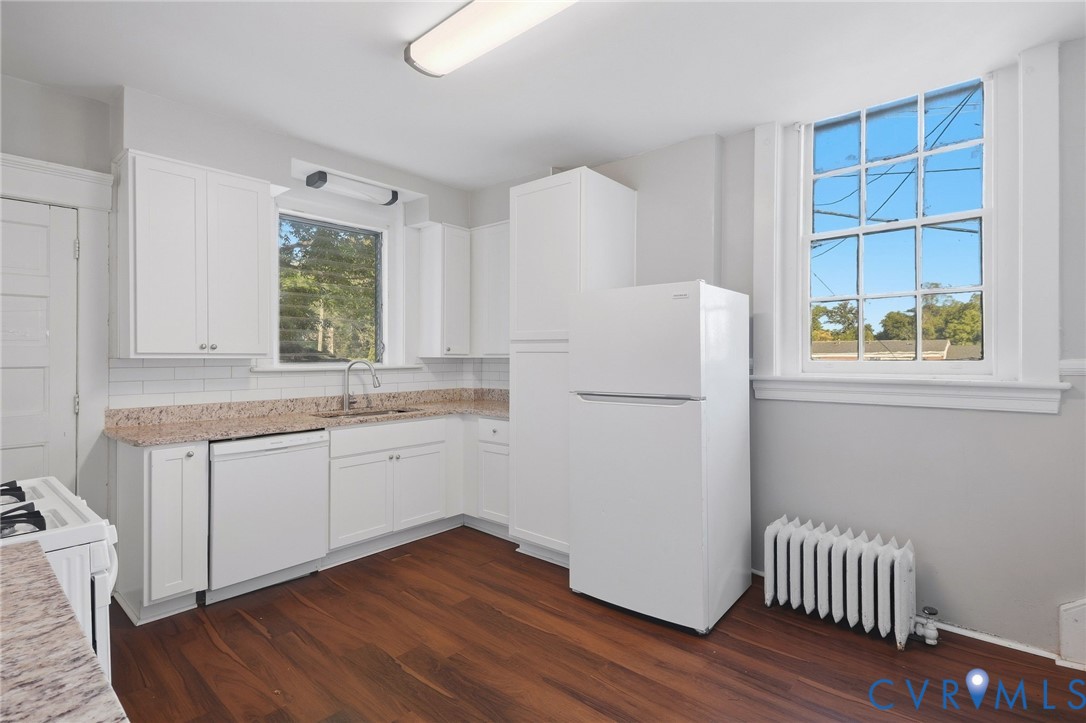 Kitchen featuring white cabinetry, granite-look countertops, white subway tile backsplash, wood-finish flooring, and a large multi-pane window Kitchen featuring white cabinetry, granite-look countertops, white subway tile backsplash, wood-finish flooring, and a large multi-pane window