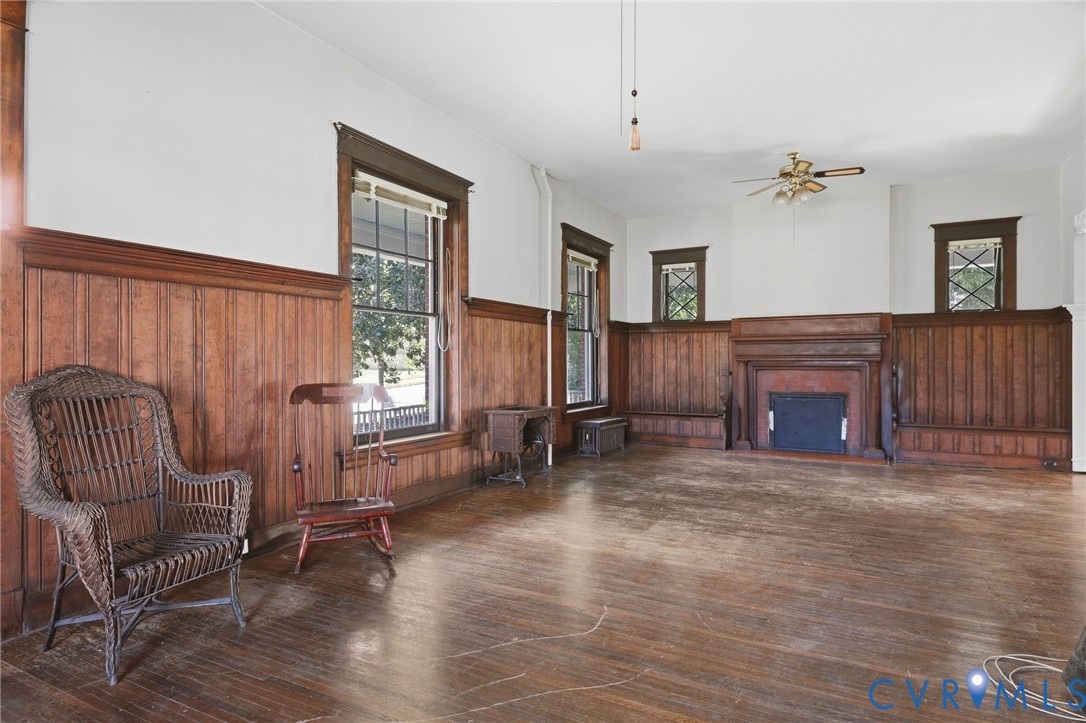 Wood-finish flooring, wood paneling, decorative fireplace, multiple windows, and a ceiling fan Wood-finish flooring, wood paneling, decorative fireplace, multiple windows, and a ceiling fan
