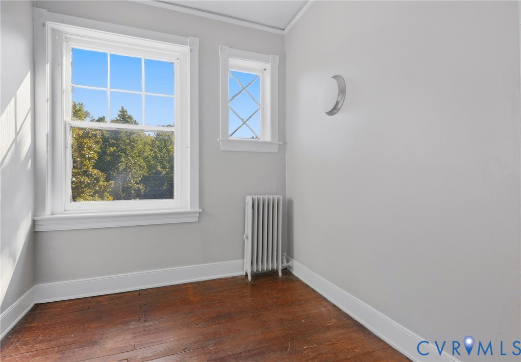 Hardwood flooring with white trim, multiple windows with white casing, and a vertical radiator