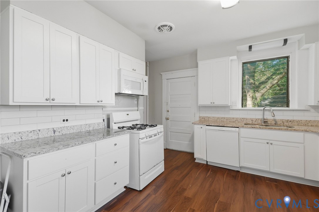 Kitchen featuring white cabinetry, light-toned countertops, a white subway tile backsplash, stainless steel sink, and wood-finish flooring