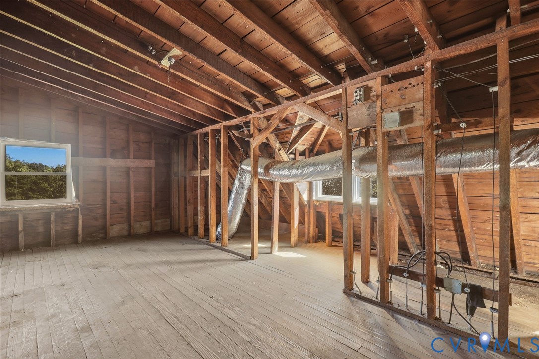 Exposed wooden ceiling rafters, exposed wood wall framing, wood-finish flooring, two windows, and exposed ductwork