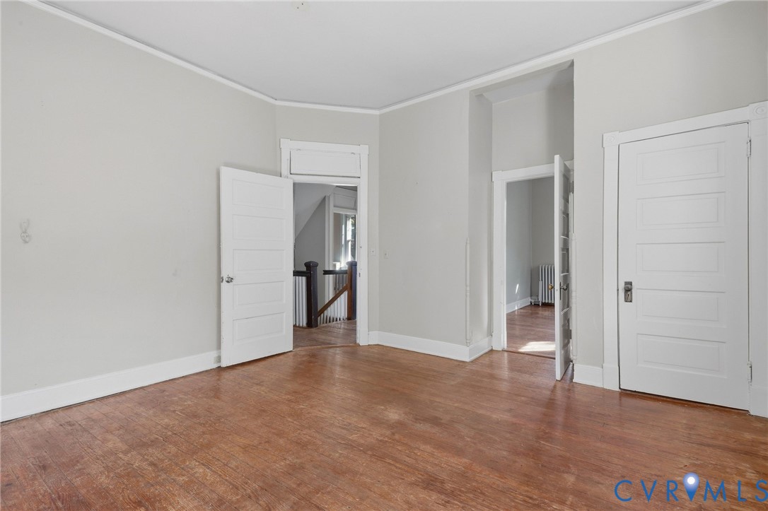 Wood-finish flooring with white trim, five-panel interior doors, and a staircase with dark wood newel post and balusters