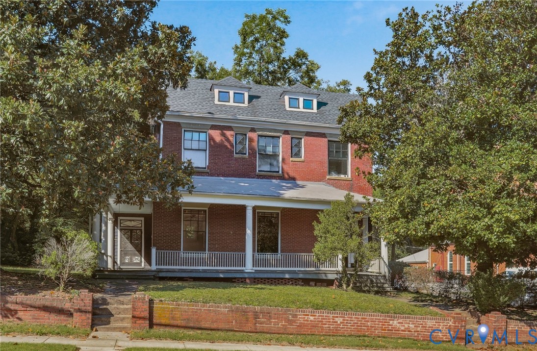Brick exterior with a slate-style roof, multiple dormer windows, covered front porch, and a brick retaining wall