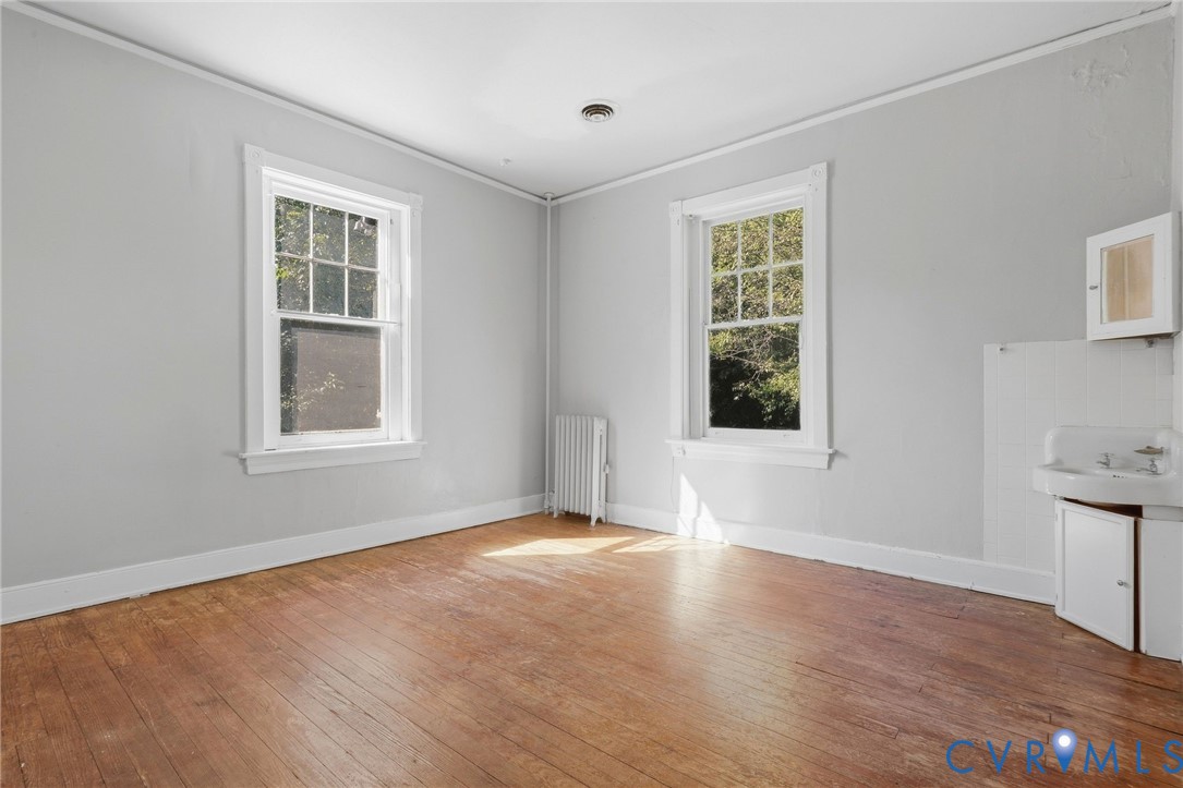 Hardwood flooring, two large windows, baseboard heating unit, wall-mounted sink, and cabinetry