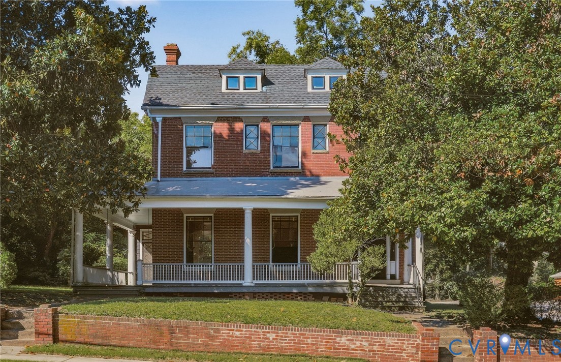 Two-story brick exterior featuring a covered front porch with white columns, dormer windows, and a brick retaining wall Two-story brick exterior featuring a covered front porch with white columns, dormer windows, and a brick retaining wall