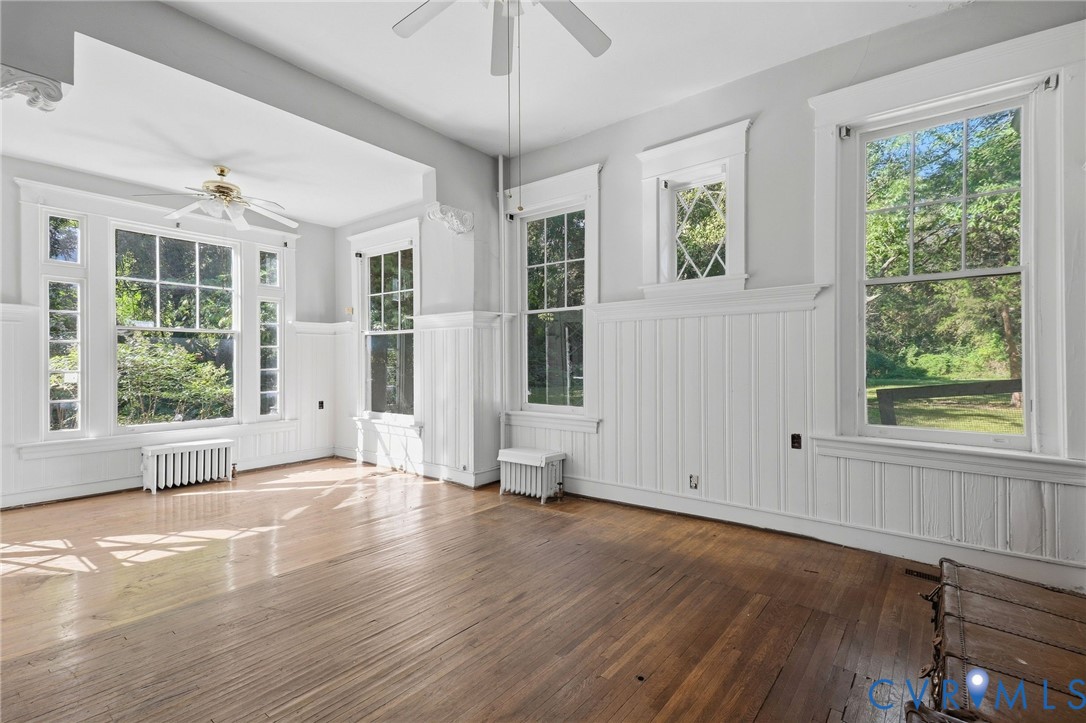 Hardwood flooring, paneled wainscoting, multiple large windows, window trim detail, and ceiling fans