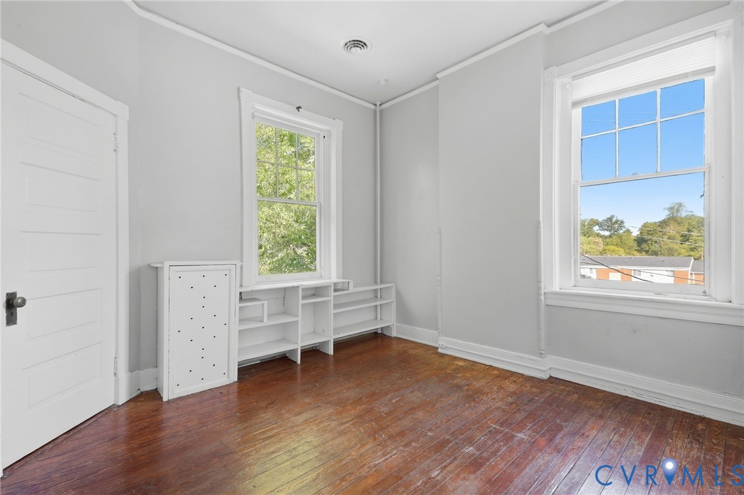 Hardwood flooring, painted paneled door, built-in shelving, white trim, and two double-hung windows