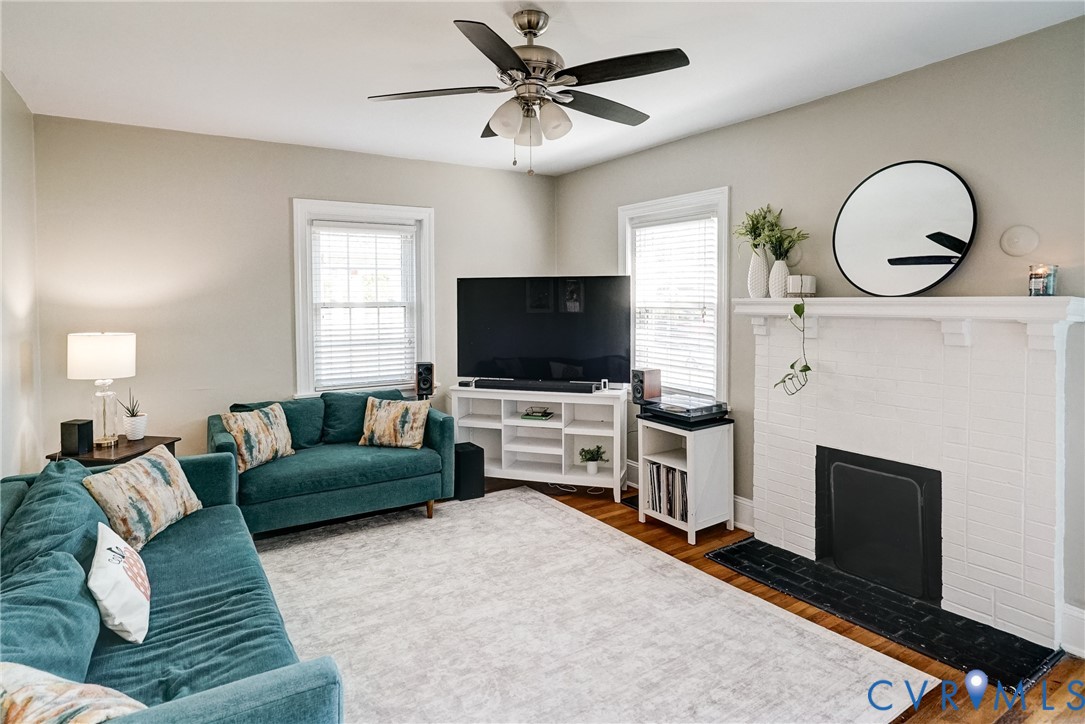 Wood-finish flooring, white trim, ceiling fan, white fireplace with black surround, and built-in media console