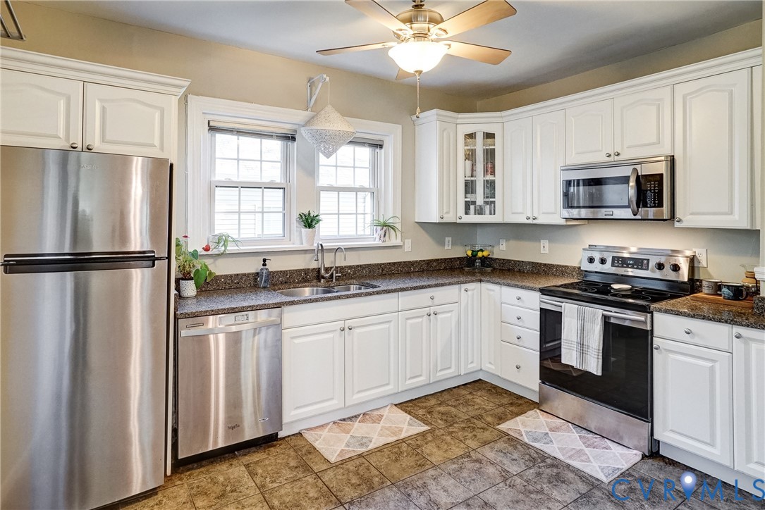 White cabinetry, stainless steel appliances, granite-look countertops, tiled flooring, and a ceiling fan with integrated lighting