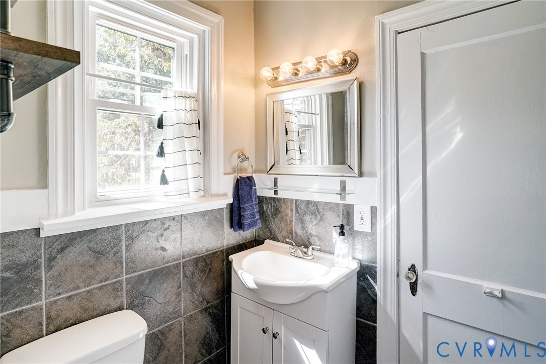 White vanity with integrated sink, silver-framed mirror, four-bulb vanity lighting, and tiled wainscoting