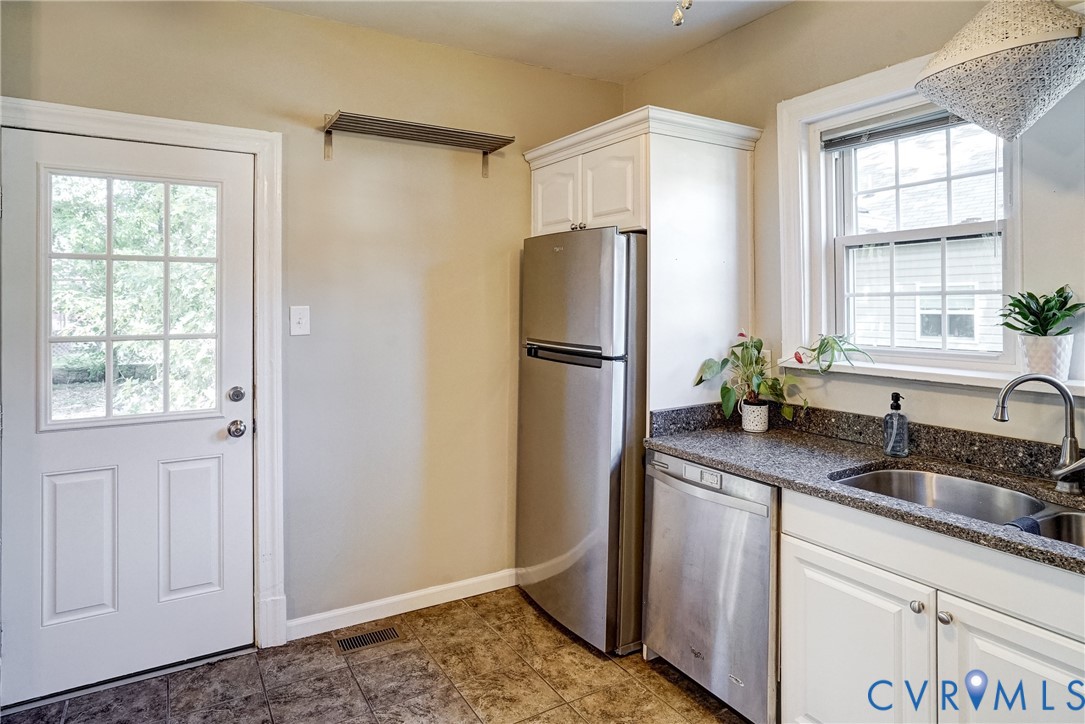 White paneled exterior door with divided light window, tiled flooring, stainless steel refrigerator, stainless steel dishwasher, and a double basin sink with a window above