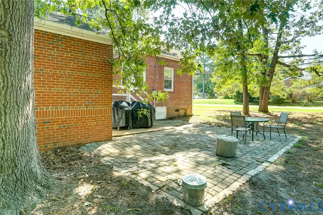 Brick exterior with white trim, paver patio, and mature trees