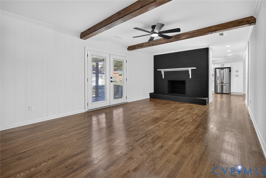 Interior space featuring wood-finish flooring, exposed ceiling beams, a floor-to-ceiling painted brick fireplace with a mantle, and glass-paned double doors