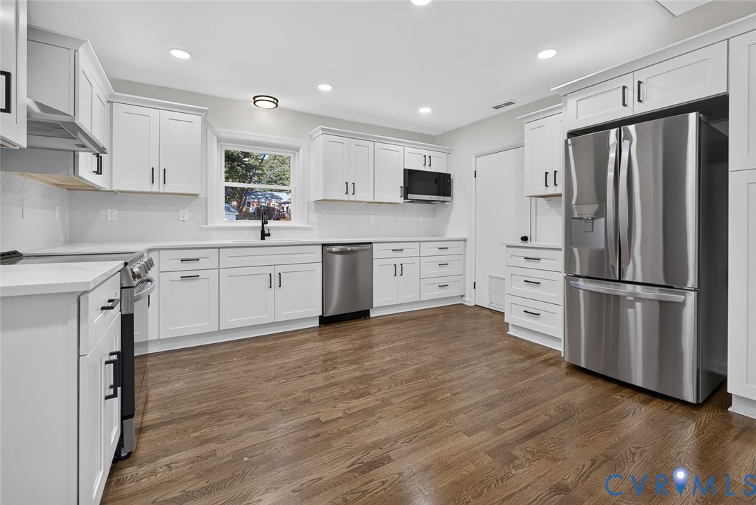 Kitchen featuring white shaker-style cabinetry, stainless steel appliances, wood-finish flooring, recessed lighting, and solid-surface countertops