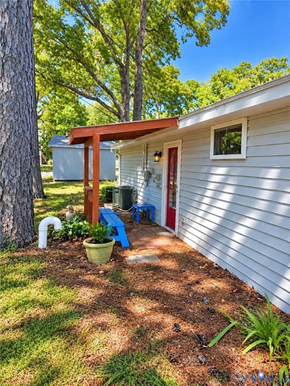 Exterior featuring light grey siding, a red entry door, a covered porch entrance with a wooden pergola, and a single window with white trim