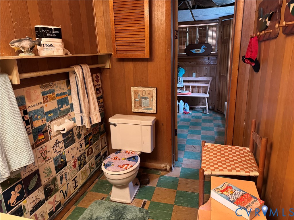 Bathroom featuring wood-paneled walls, checkerboard-patterned flooring, and a decorative tile accent wall