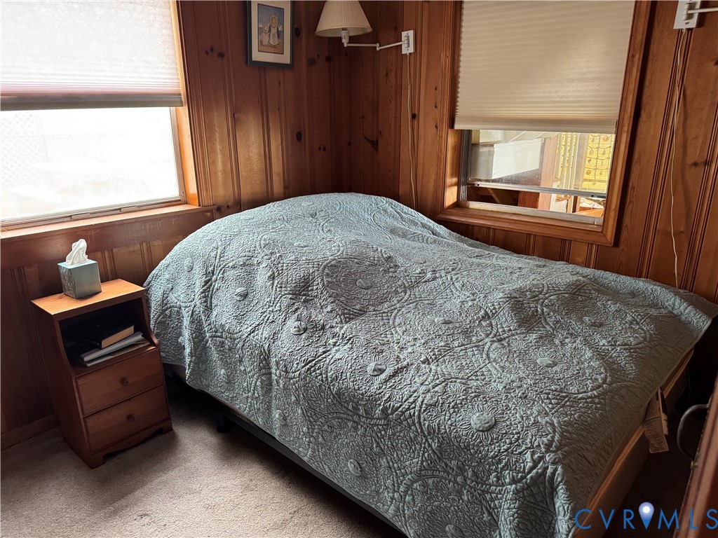 Wood-paneled walls, two windows with pleated cellular shades, and wall-mounted swing-arm lamp