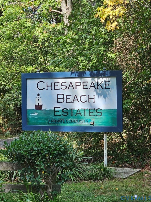 "Chesapeake Beach Estates" community signage with a lighthouse graphic, framed by mature trees and manicured shrubbery