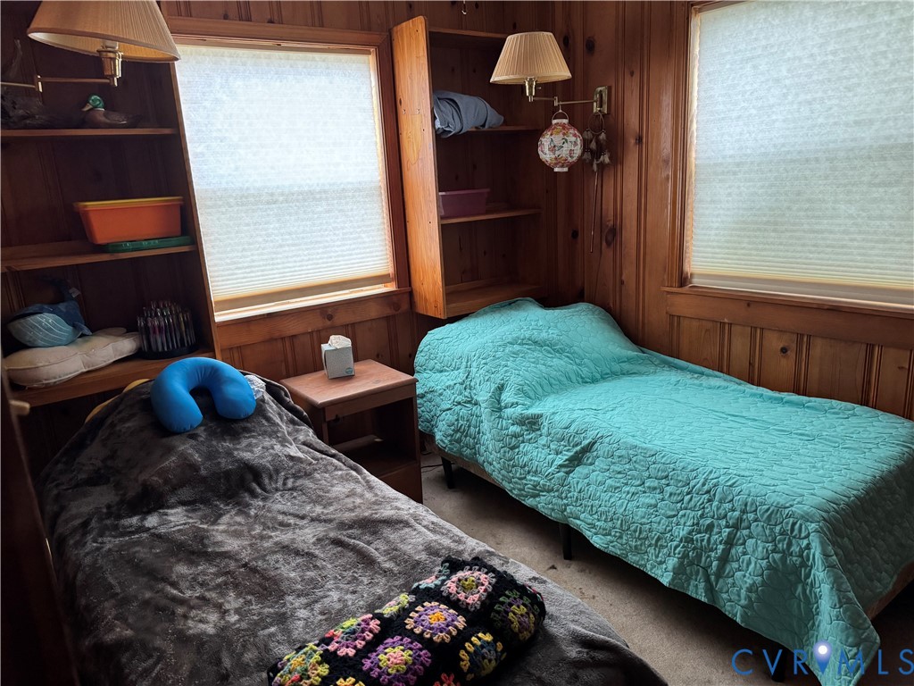 Wood-paneled interior walls, two windows with integrated cellular shades, built-in shelving units, and two wall-mounted adjustable lamps