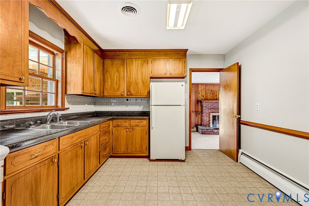 Kitchen featuring wood cabinetry, laminate countertops, a tile backsplash, and a double basin sink with a chrome faucet Kitchen featuring wood cabinetry, laminate countertops, a tile backsplash, and a double basin sink with a chrome faucet