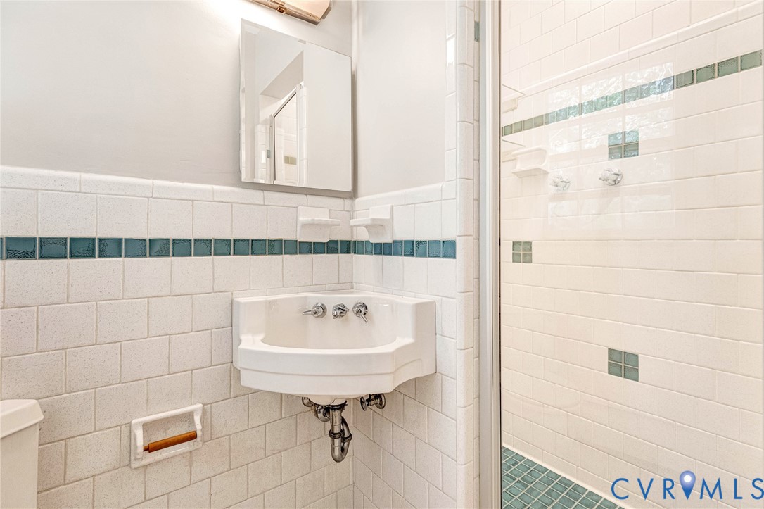Corner sink vanity with white tile walls featuring a decorative teal accent band
