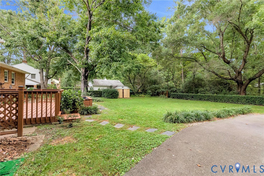 Expansive backyard featuring a wood deck, manicured lawn, stepping stones, and mature trees