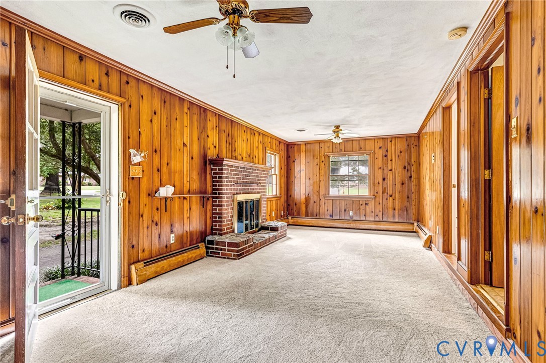 Wood paneling throughout, brick fireplace with hearth, and wall-mounted baseboard heating