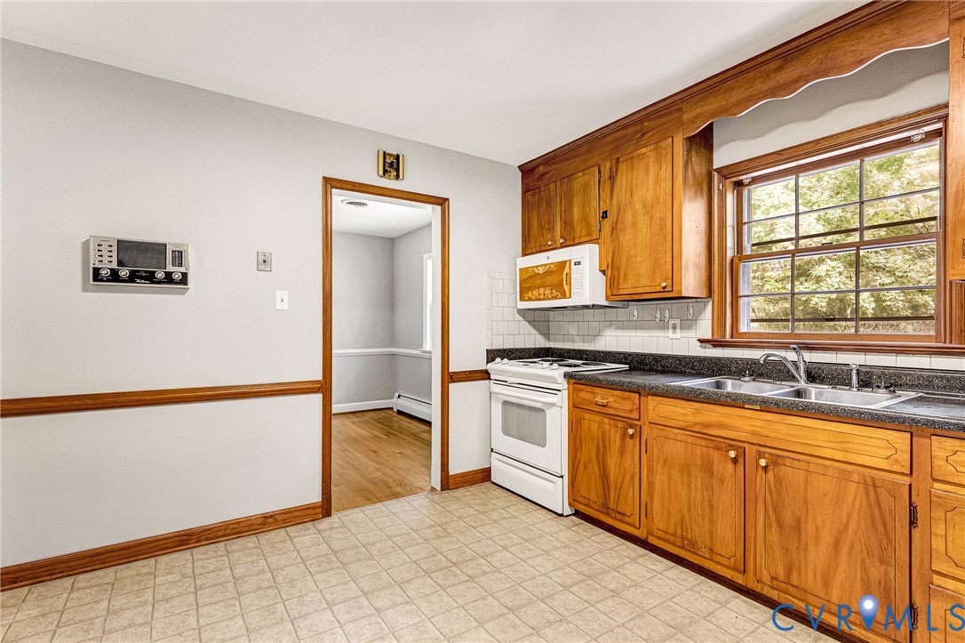 Wood-finish cabinetry with a double basin sink, white tile backsplash, and light-toned flooring Wood-finish cabinetry with a double basin sink, white tile backsplash, and light-toned flooring
