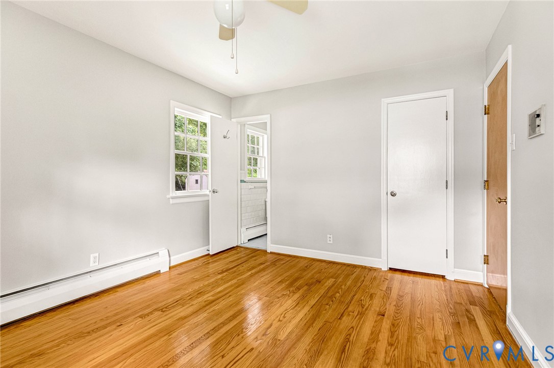 Wood-finish flooring, neutral wall tones, white trim, window with exterior views, and a ceiling fan