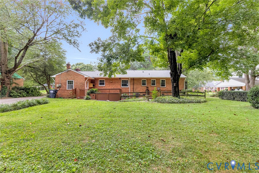 Expansive lawn area with mature trees, brick exterior, and a wood deck