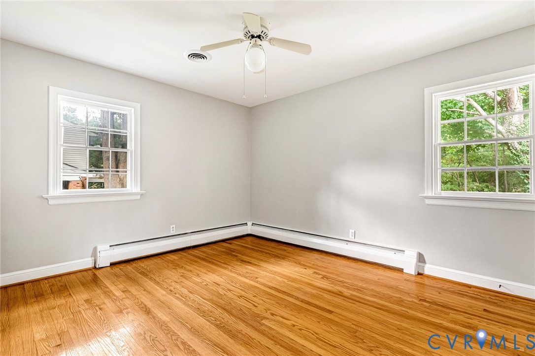 Hardwood flooring, two large windows, white walls, ceiling fan with integrated lighting, and white trim